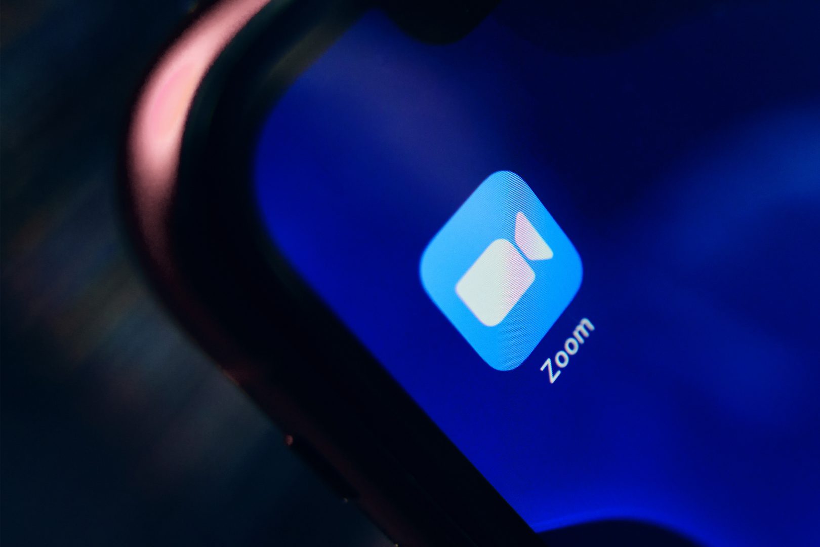 The app icon for the video-conferencing app Zoom is featured on a phone screen held in the hand of an unknown person.