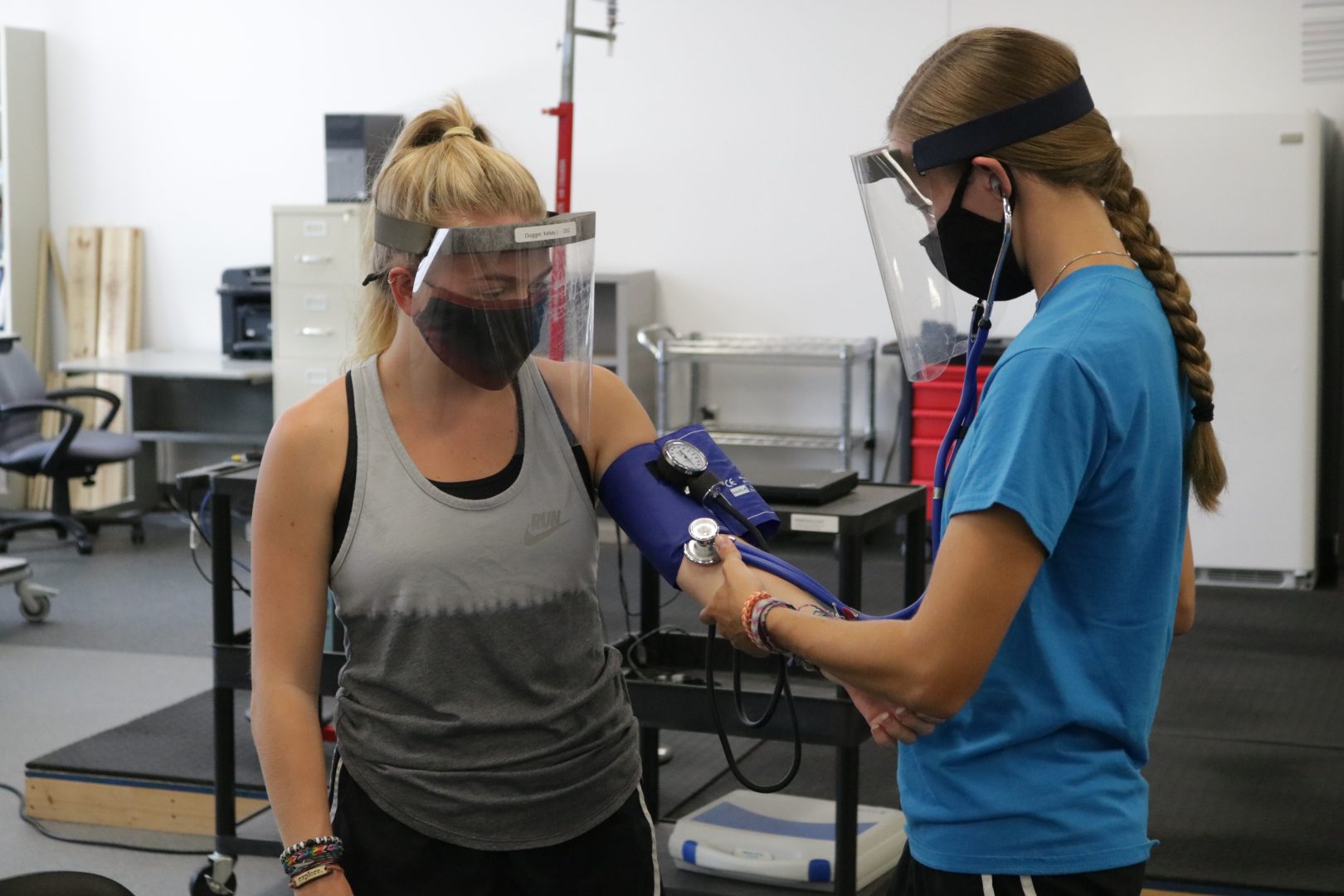 Junior exercise science major Melissa Spencer takes the blood pressure or her classmate junior and exercise science major Kelsey Dugger. Although their class meets in person, they are required to wear full PPE with face masks and face shields while in the classroom.