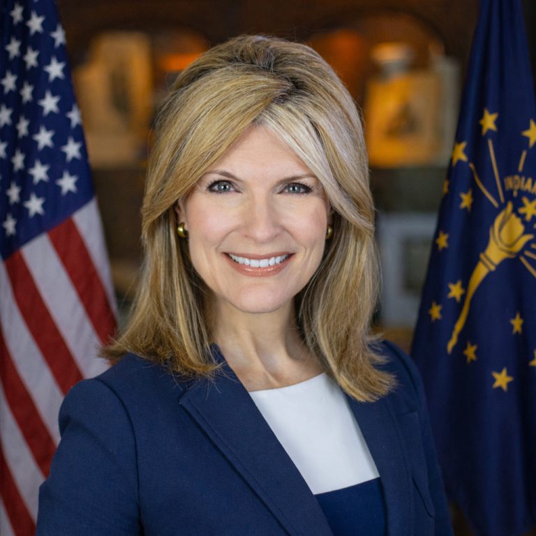 Elise Nieshalla standing and smiling between the US and Indiana state flags